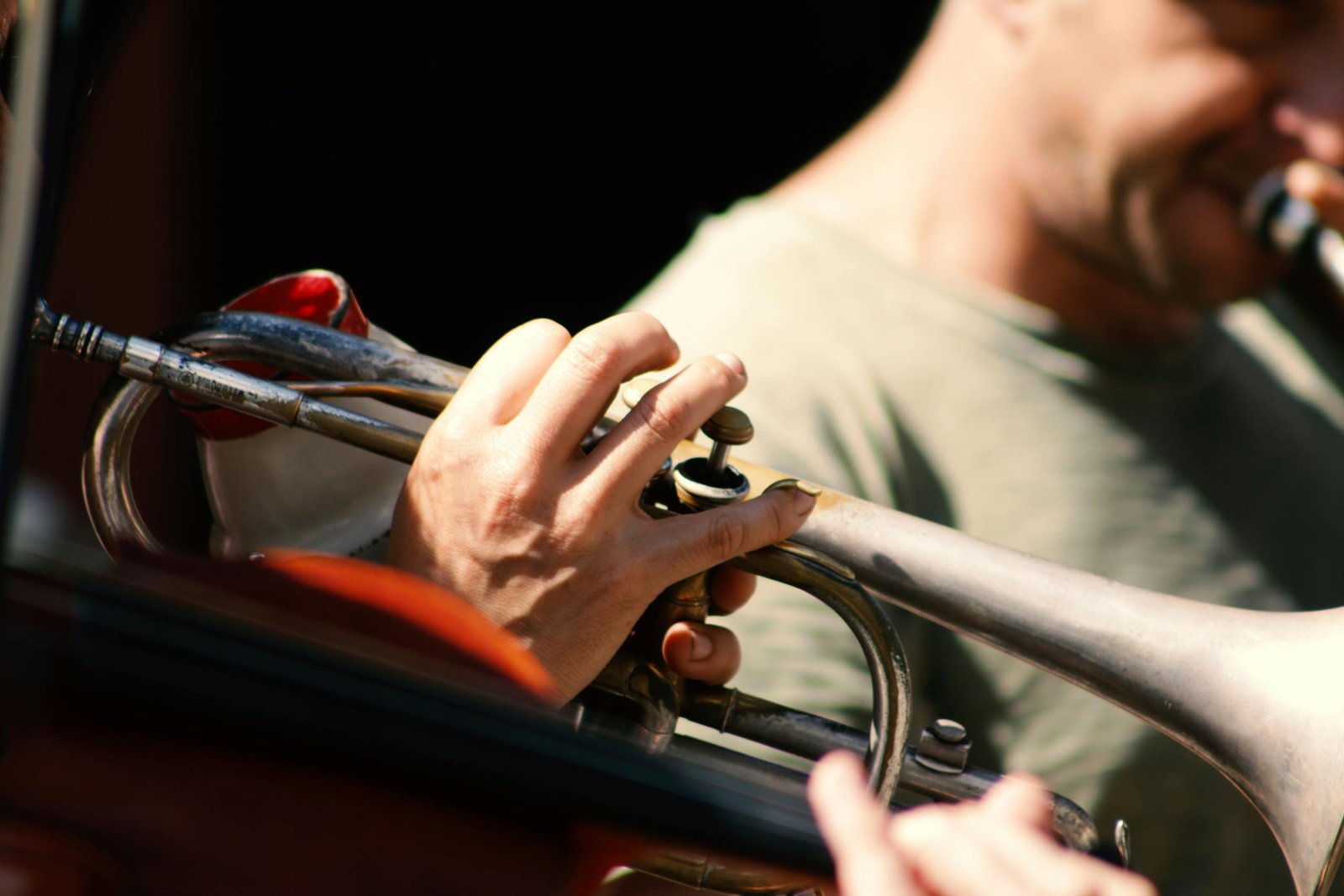 A close-up of a male musician playing a trumpet during a sunny outdoor performance.